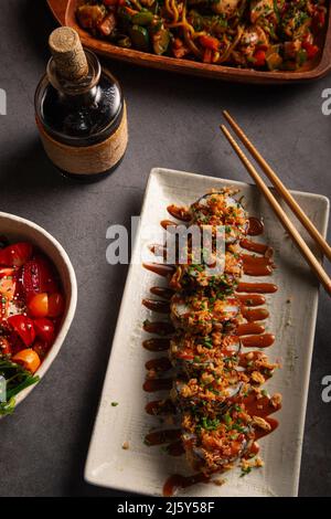 Von oben leckere Tempura Sushi-Brötchen mit gebratener Zwiebel serviert auf weißem Teller mit Sauce und Essstäbchen im Restaurant Stockfoto
