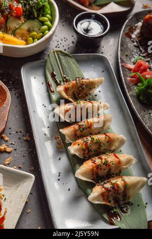 Von oben von leckeren traditionellen Jiaozi mit Sauce serviert auf dem Teller mit grünen Blatt auf dem Tisch mit verschiedenen Gerichten in hellen Restaurant Stockfoto