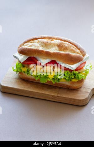 Leckeres Sandwich mit Hühnchen auf Salat und Tomatenscheiben mit Käse auf Holzbrett auf grauem Hintergrund in der Küche serviert Stockfoto