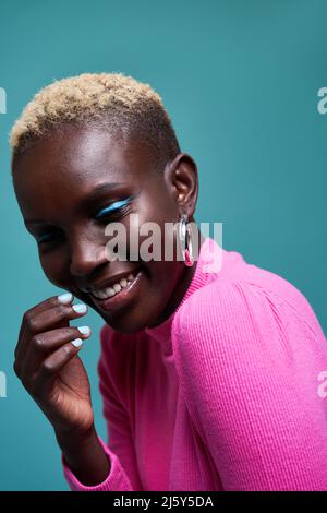 Nahaufnahme einer fröhlichen Afrikanerin mit kurzen Haaren in einer Studioaufnahme mit blauem Hintergrund Stockfoto