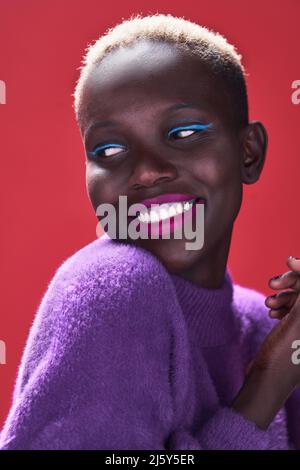 Nahaufnahme einer fröhlichen Afrikanerin mit kurzen Haaren in einer Studioaufnahme mit rotem Hintergrund Stockfoto