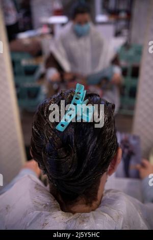 Junge Frau mit Haarspange auf dem Kopf, die vor dem Spiegel wartet, während der Haarfärbestoff trocknet Stockfoto