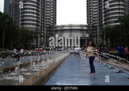 KUALA LUMPUR, MALASIA – 26. JANUAR 2020 Menschen spielen in den Wasserfontänen am Fuße der Petronas Twin Towers Stockfoto