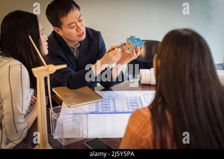 Ingenieure mit Haus- und Windenergieanlagenmodell sprechen in Meetings Stockfoto