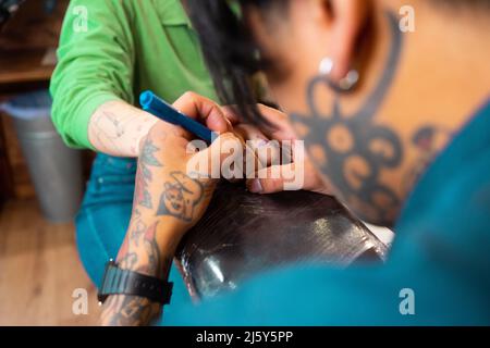 Crop gesichtslose tätowierte Meister mit schwarzen Haaren Zeichnung Tattoo Entwurf auf Finger des anonymen Kunden mit Stift in professionellen Licht Salon Stockfoto