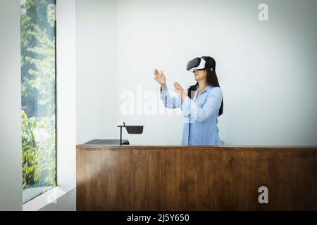 Geschäftsfrau, die im Büro ein VR-Headset hinter dem Schreibtisch verwendet Stockfoto