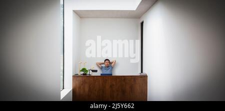 Männlicher Ingenieur mit Händen hinter dem Kopf am Schreibtisch bei Modellen mit Windenergieanlagen Stockfoto