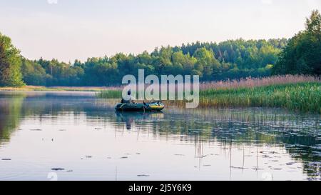 Region Minsk, Weißrussland - 09. Juni 2020: Fischer auf einem Boot am frühen Morgen auf einem See, der im Schilf fischt Stockfoto