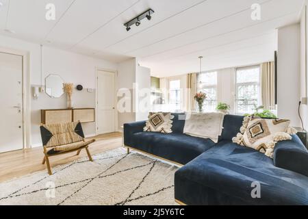 Bequemes Sofa auf Teppich neben Sessel an der Wand und Schrank mit Blumen in hellen stilvollen Wohnzimmer mit dekorativen Rahmen platziert Stockfoto