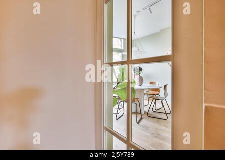 Durch Glastür der Küche mit Stühlen am runden Tisch in hellen geräumigen Esszimmer mit grünen Topfpflanze in der Wohnung platziert Stockfoto