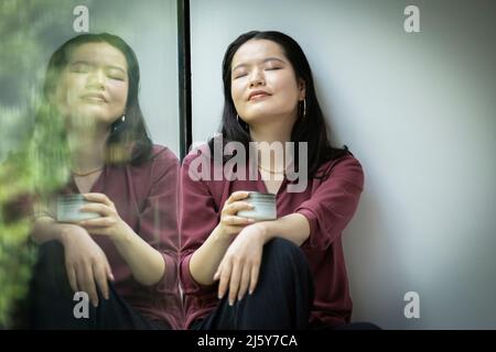 Ruhige junge Frau, die im Fenster Tee trinkt Stockfoto