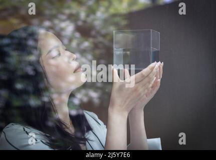 Nahaufnahme einer Designerin, die den Würfel mit Flüssigkeit am Fenster betrachtet Stockfoto