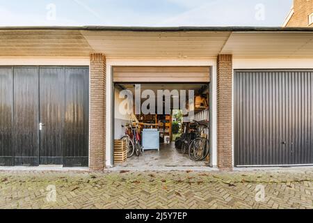 Geöffnete Metall-Garage mit geparkten Fahrrädern und Holzkisten mit verschiedenen Geräten auf Regalen in der Landschaft am Sommertag gelegen Stockfoto