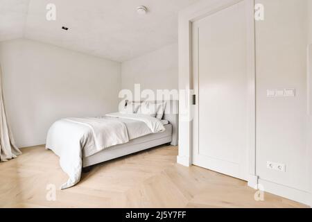 Komfortables Bett mit Decke und Kissen im hellen, geräumigen Schlafzimmer mit weißer Tür Stockfoto