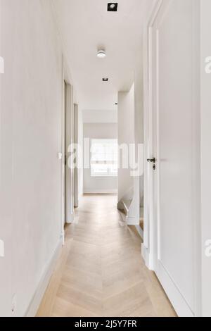 Leerer, enger Flur mit weißen Wänden und Türen und beigefarbenem Laminatboden im Haus Stockfoto