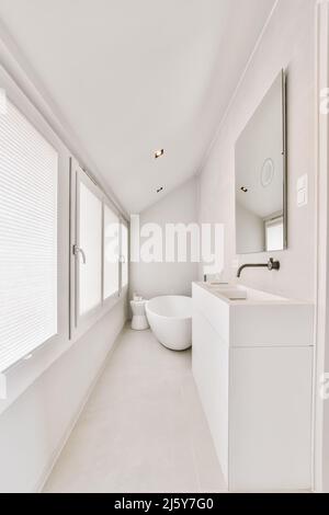 Waschbecken an der Wand mit Spiegel in der Nähe von Keramik-Badewanne im hellen modernen Badezimmer mit Fenstern und weißen Wänden zu Hause platziert Stockfoto