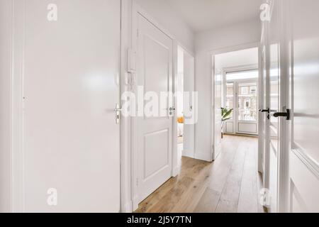 Leerer enger Flur mit weißen Wänden und Türen und Holzlaminatboden im Haus Stockfoto