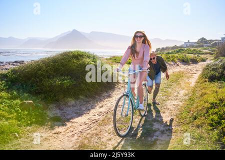 Unbeschwertes Paar, das auf dem sonnigen Sommerstrand Fahrrad fährt Stockfoto