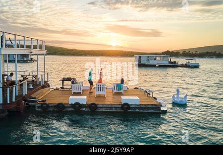 Unbeschwertes Paar, das bei Sonnenuntergang auf der Terrasse des Hausbootes auf dem See tanzt Stockfoto