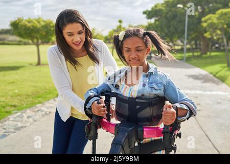 Mutter hilft behinderten Tochter zu Fuß in Rollator im Park Stockfoto