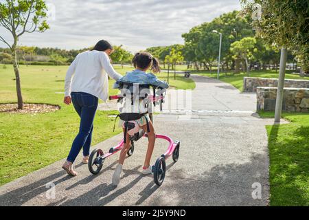 Mutter und behinderte Tochter mit Rollator zu Fuß in sonnigen Park Stockfoto