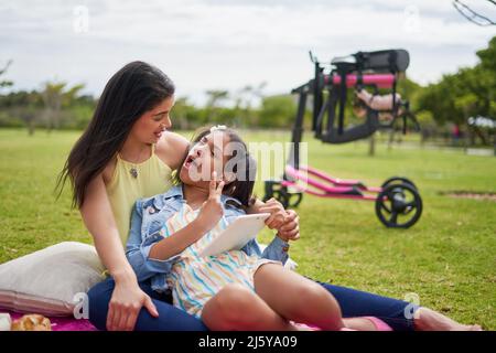 Mutter und behinderte Tochter mit digitalem Tablet auf einer Decke im Park Stockfoto