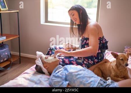 Mutter gibt einer behinderten Tochter zu Hause eine Gesichtsbehandlung auf dem Bett Stockfoto