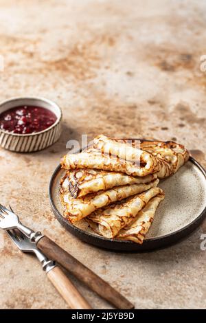 Crepes in brauner Platte. Frühstück Zusammensetzung mit Blinis, rustikale Gabeln, Marmelade. Vertikale Ausrichtung. Speicherplatz kopieren Stockfoto