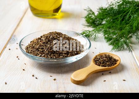 Rohe Dillsamen auf einer Glasuntertasse und Holzlöffel in der Nähe von frischem grünen Dill. Kochen mit natürlichen Gewürzen und Gewürzen. Anethum graveolens Samen Stockfoto