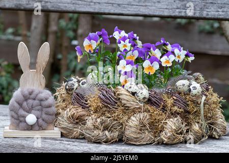 osterdekoration mit osterhasen- und Viola-Blumen in Kranz aus Moos, Ästen und Stroh Stockfoto