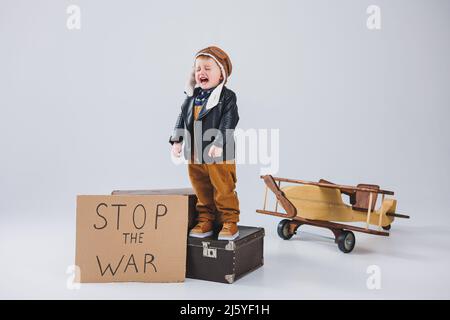 Ein kleiner Junge in einer Lederjacke mit einem Schild, um den Krieg zu stoppen. Holzflugzeug mit umweltfreundlichem Material Stockfoto