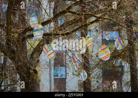 Olaine, Lettland - 18. April 2022. Städtisches Landschaftsdesign mit Osterdekoren in einer Stadt. Bunte Deko-Eier auf Ästen vor dem Haus. Stockfoto