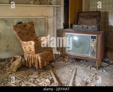 Alter Fernseher und Stuhl in einem verlassenen Haus. Stockfoto