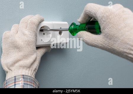 Ein Mann, der eine Steckdose mit einem Schraubendreher verschraubt. Hochwertige Fotos Stockfoto