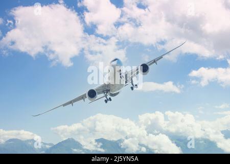 Landeanflug eines Flugzeugs mit ausgefahrenen Fahrrädern, die sich in der Luft vor dem Hintergrund hoher malerischer Berge drehen Stockfoto