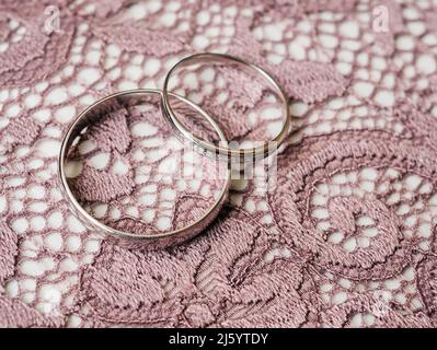 Klassische Eheringe liegen auf dem braunen Spitzenhintergrund in Nahaufnahme Stockfoto