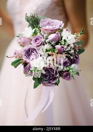 Lila Hochzeitsstrauß in den Händen des Brautpapartys, Nahaufnahme. Violette Blumen, lila klassisches Hochzeitskleid, rosig Spitze Kleid. Stockfoto