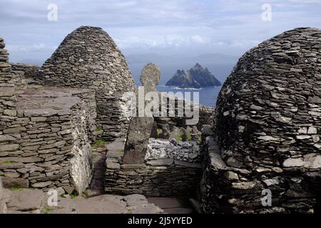 Blick auf den kleinen Skelig von Skelig Michael, keltisches Kreuz und steinerne Bienenhaus-Hütten im Vordergrund Stockfoto