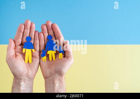 Hände mit separater Familie auf Papier mit ukrainischem Flaggenkleid auf gelbem und blauem Hintergrund. Speicherplatz kopieren. Die Zahlen sind auf Papier ausgeschnitten. Stockfoto