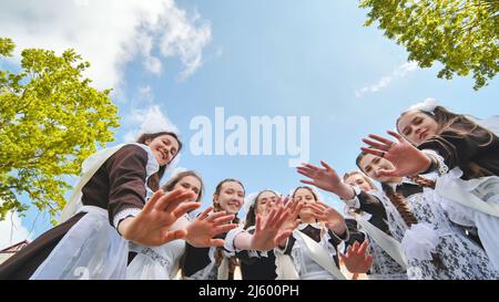 Glückliche russische Schulabgänger strecken sich an ihrem letzten Schultag die Hände. Stockfoto