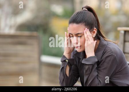 Gestresster Teenager, der an Migräne leidet und sich auf einer Bank in einem Park beschwert Stockfoto