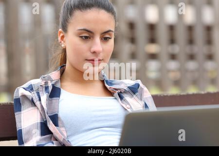 Teen prüft Laptop-Inhalte auf einer Bank in einem Park sitzen Stockfoto