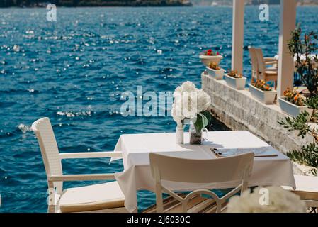 Blick auf die Straße auf eine Terrasse am Wasser mit Tischen und Stühlen im Restaurant im historischen Dorf Perast in der Bucht von Kotor, Montenegro. Sommerurlaub Stockfoto