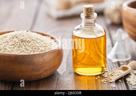 Sesamsamen in der Schüssel und eine Flasche Sesamöl auf dem Holztisch. Stockfoto