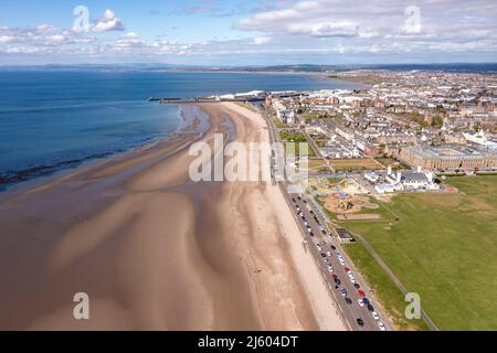 Ayr, Schottland, Großbritannien. 26. April 2022. IM BILD: Luftdrohnenansicht von oben auf den Ayr Beach mit Blick auf den Firth of Clyde und die Küstenstadt Ayr. Westlich von Schottland sah man strahlenden Sonnenschein und blauen Himmel an der Küste am Ayr Beach. Menschen gehen spazieren und ein Reiter nimmt ihr Pferd durch einen Galopp im kühlen Meerwasser. Quelle: Colin Fisher/Alamy Live News Stockfoto