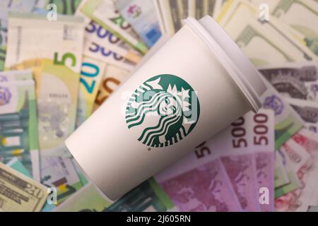 KHARKIV, UKRAINE - 16. DEZEMBER 2021: Weißer Papierbecher mit Starbucks Logo und Geldscheinen. Starbucks ist das größte Kaffeehaus der Welt mit über 20, Stockfoto