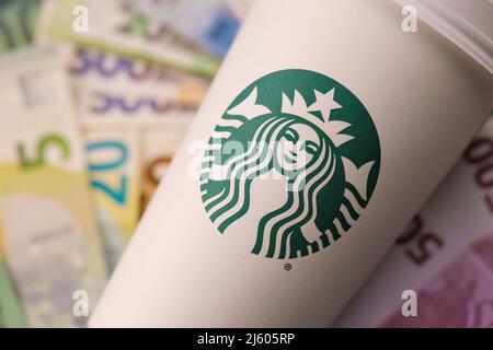 KHARKIV, UKRAINE - 16. DEZEMBER 2021: Weißer Papierbecher mit Starbucks Logo und Geldscheinen. Starbucks ist das größte Kaffeehaus der Welt mit über 20, Stockfoto