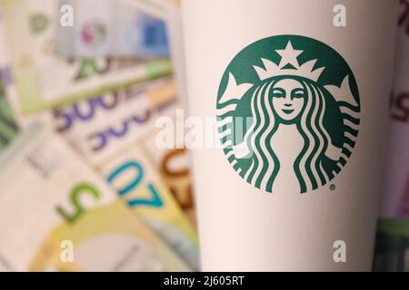 KHARKIV, UKRAINE - 16. DEZEMBER 2021: Weißer Papierbecher mit Starbucks Logo und Geldscheinen. Starbucks ist das größte Kaffeehaus der Welt mit über 20, Stockfoto