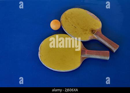 Gelbe Tischtennisschläger und orangefarbener Ball auf blauem Tisch, flach liegend. Kopierbereich, horizontal Stockfoto