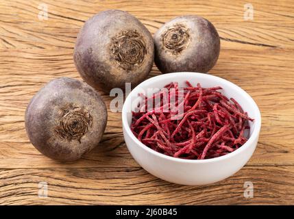 Rote Beete und rote Beete, im Julienne-Stil in einer Schüssel über einem Holztisch. Stockfoto